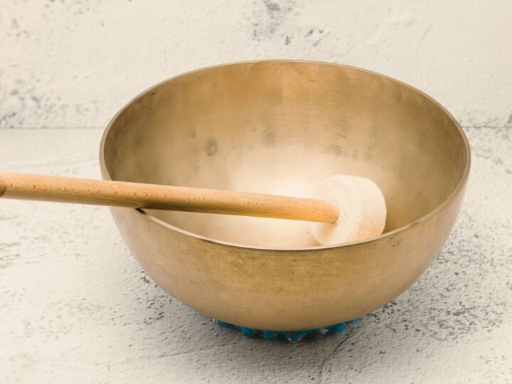 A hammered metal singing bowl resting on a ring cushion, with a wooden mallet lying across it